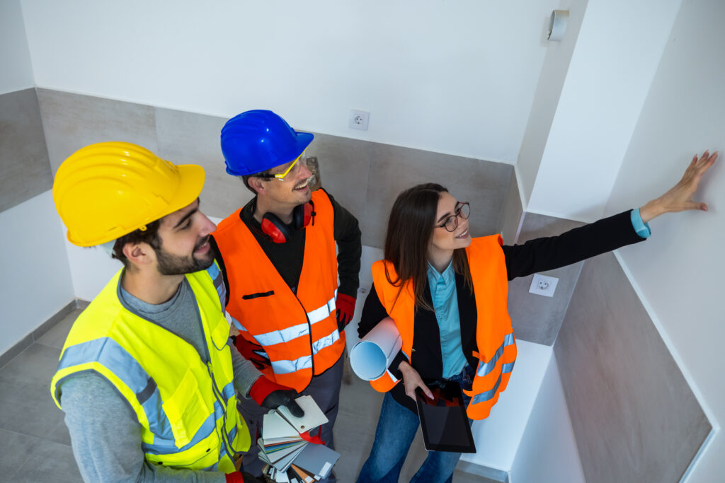 Three construction workers in bathroom choosing tile colors using color palette blueprint and tablet.